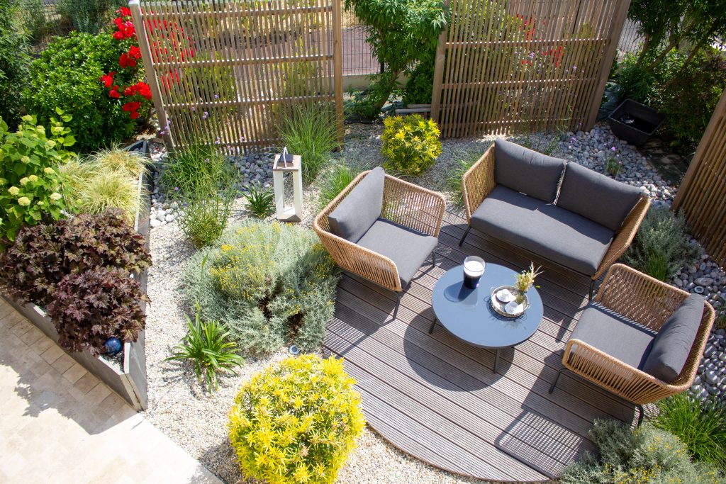 Terrasse en bois paysagée par des massifs minéraux et décorée d'un élégant mobilier de jardin.
