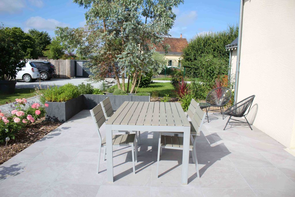 Terrasse moderne paysagée en dalles de grès cérame grises.